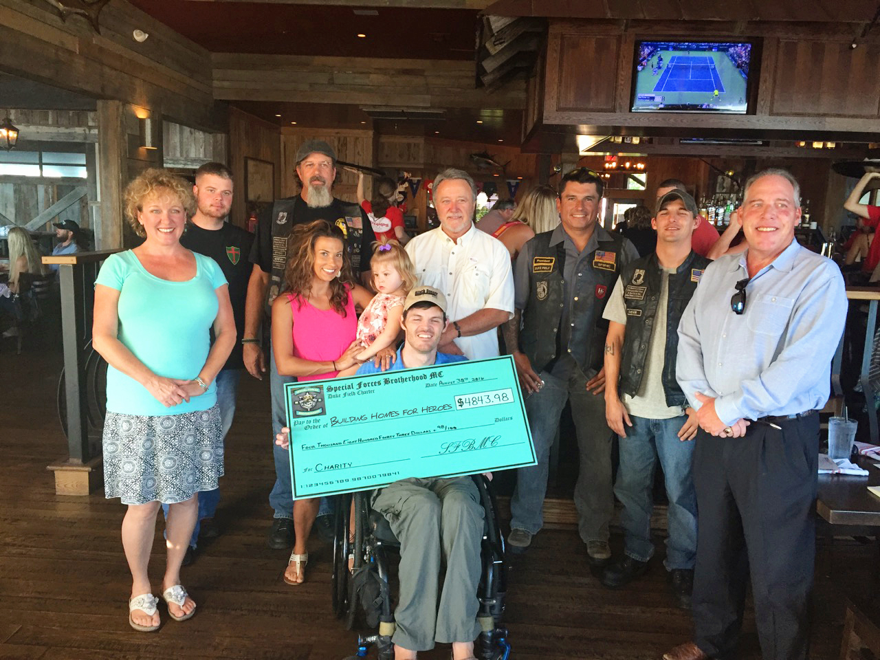 Military Motorcycle Club members presenting a large check to a man in a wheelchair