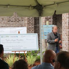Randy Wise speaking next to a large check